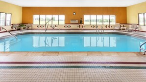 An indoor swimming pool with clear blue water, surrounded by beige and red tiled flooring, and equipped with multiple ladders and chairs.