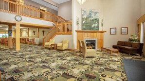 A spacious lobby with a patterned carpet, a staircase, a fireplace, and seating areas.