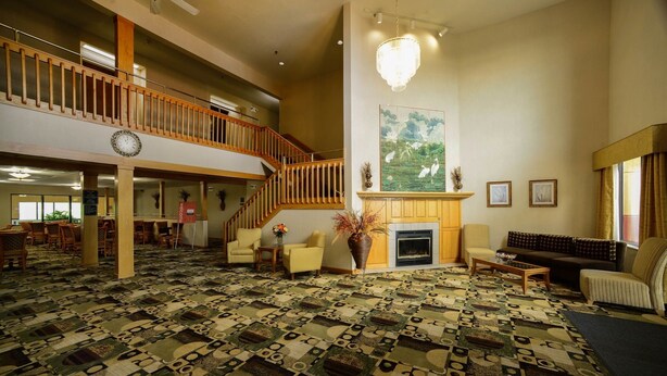 A spacious lobby with a patterned carpet, a fireplace, seating area, and a staircase.