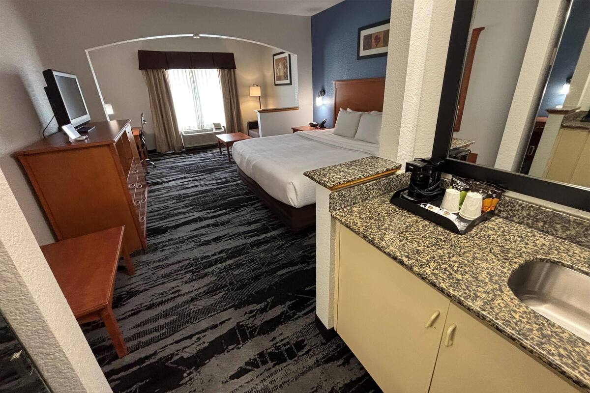 Een hotelkamer met een bed, een bureau, een stoel, een televisie, een koffiezetapparaat en een wastafel.