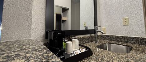 Un baño con encimera de granito, cafetera y lavamanos.