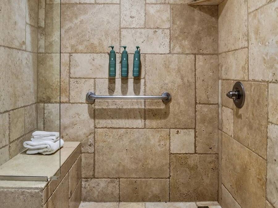 A shower area with a tiled wall, a towel rack, and a shelf.