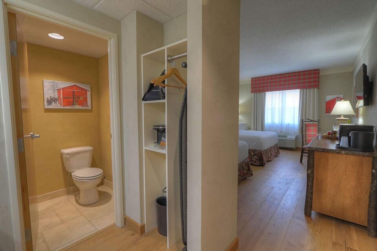 A hotel room with a bathroom, a bed, a desk, and a TV.