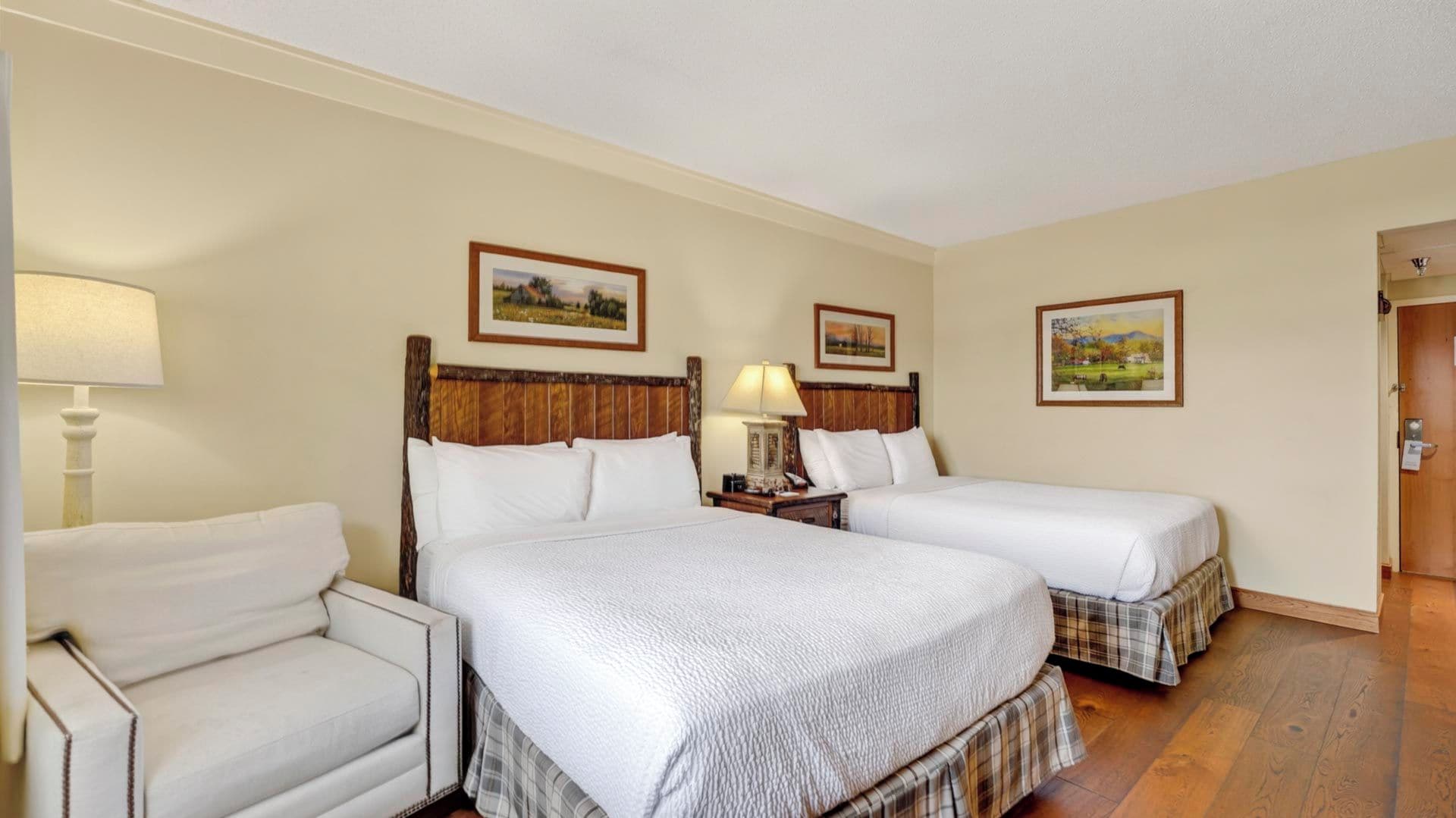 A hotel room with two beds, a chair, and a wooden floor.