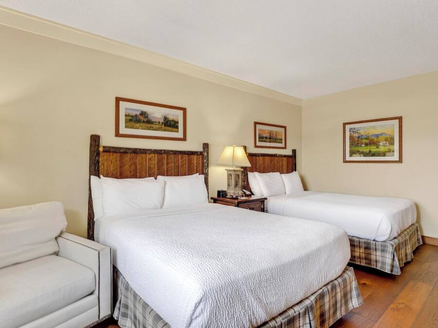 A hotel room with two beds, a chair, and a wooden floor.