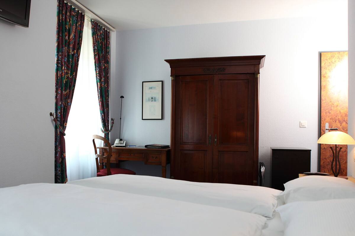 Une chambre d’hôtel avec un grand lit, un bureau avec une chaise, une armoire et une lampe.