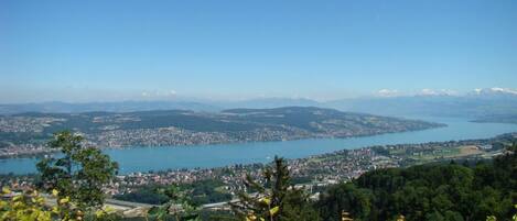 A panoramic view of a coastal town with a lake, surrounded by hills and greenery.