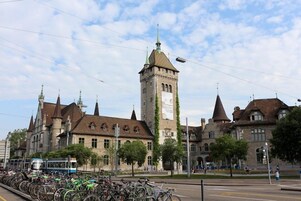 A historic building with a prominent tower, a tram line, and a row of bicycles.