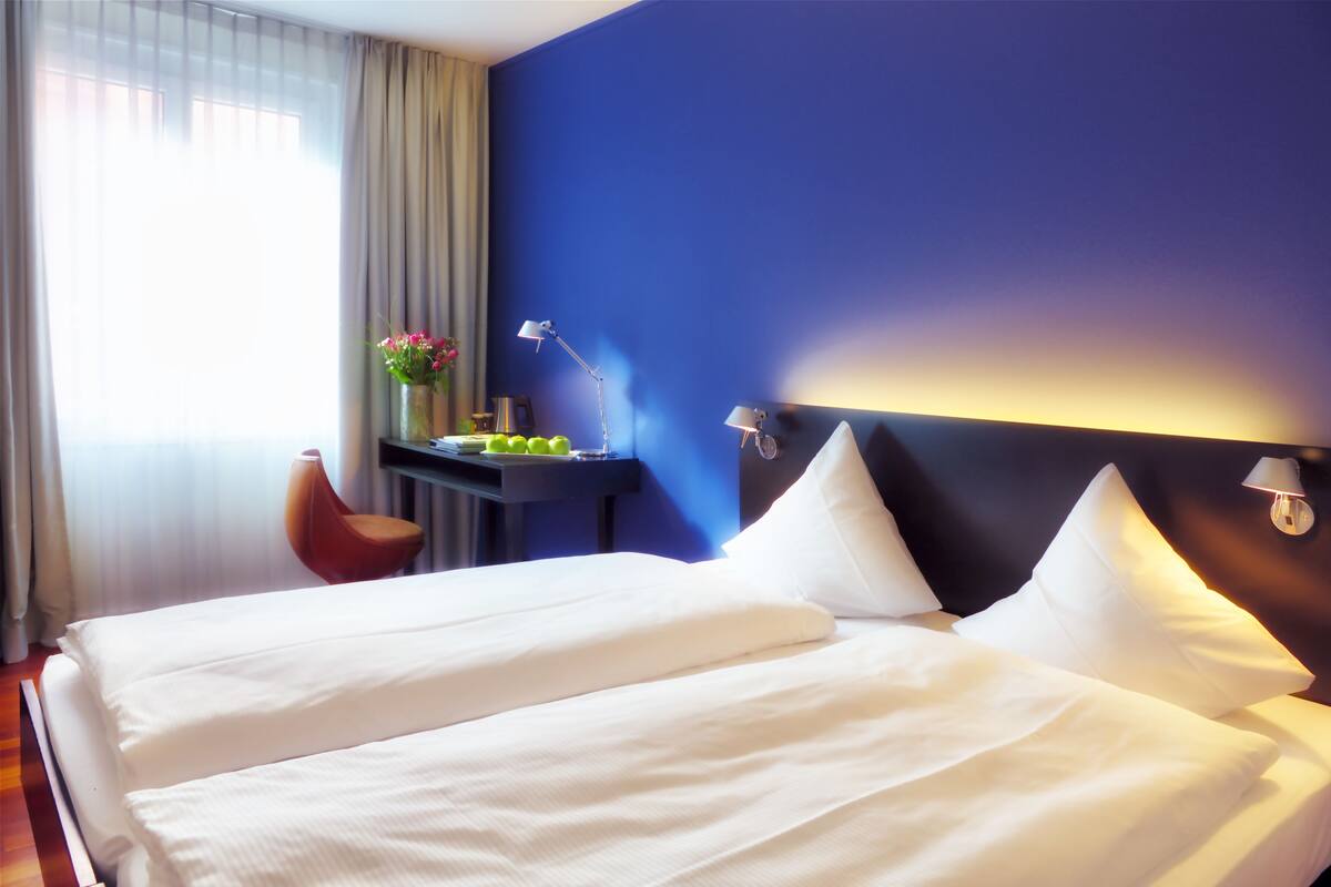Une chambre d’hôtel avec deux lits, un bureau, une chaise et une table de chevet avec une lampe.