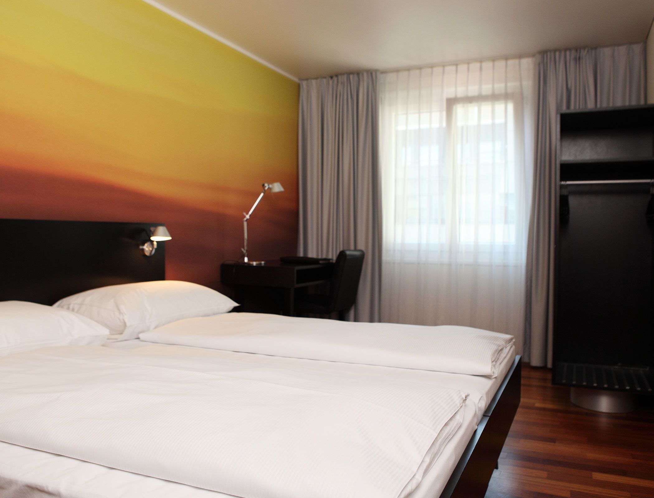 Ein Hotelzimmer mit einem großen Bett, einem Schreibtisch, einer Lampe und einem Fernseher.