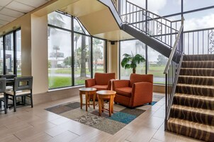 Un vestíbulo amplio con una escalera, ventanas grandes y una zona de estar con dos sillones y una mesita.