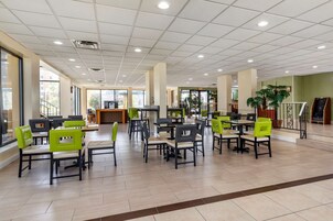 Un espacio interior amplio con varias mesas y sillas, ventanas grandes y una barra central.