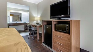 A hotel room with a bed, a desk with a chair, a television, a refrigerator, and a microwave.