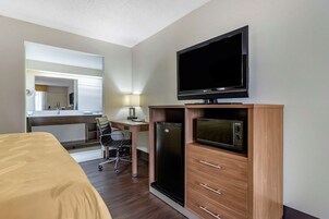 Una habitación de hotel con cama, escritorio con silla, televisor, refrigerador y microondas.