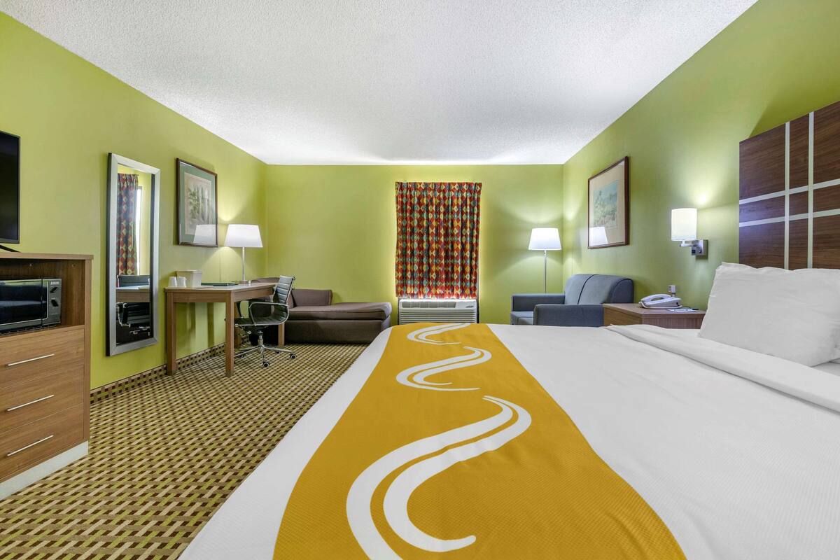 Una habitación de hotel con una cama grande, un escritorio con silla, un sofá, un televisor y un baño.