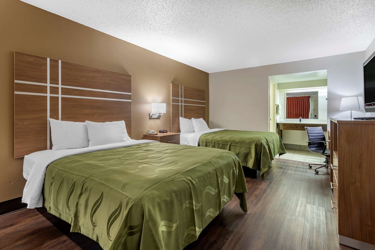 Habitación de hotel con dos camas, un escritorio, una silla y un televisor.