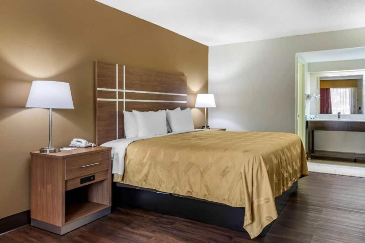 Habitación de hotel con cama, mesitas de noche, lámparas, teléfono y vistas al baño.