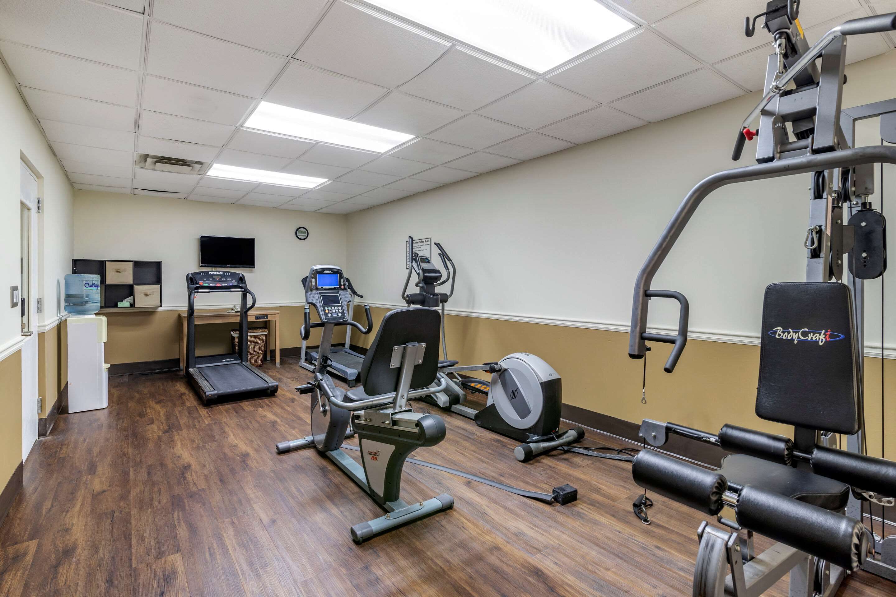 A gym with exercise equipment, a water dispenser, and a television on the wall.