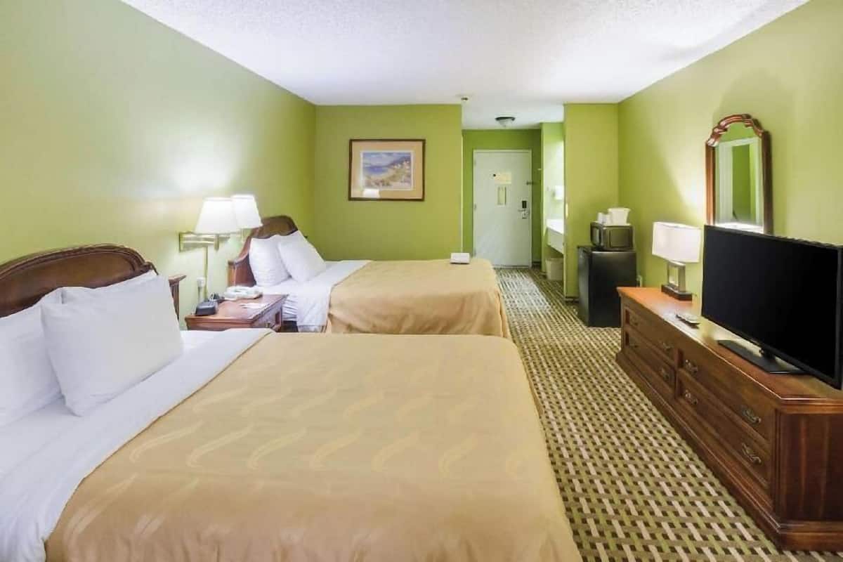 Habitación de hotel con dos camas, televisión, cómoda y un cuadro en la pared.