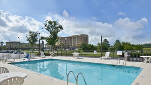 A swimming pool with lounge chairs and tables, surrounded by a fence and trees.