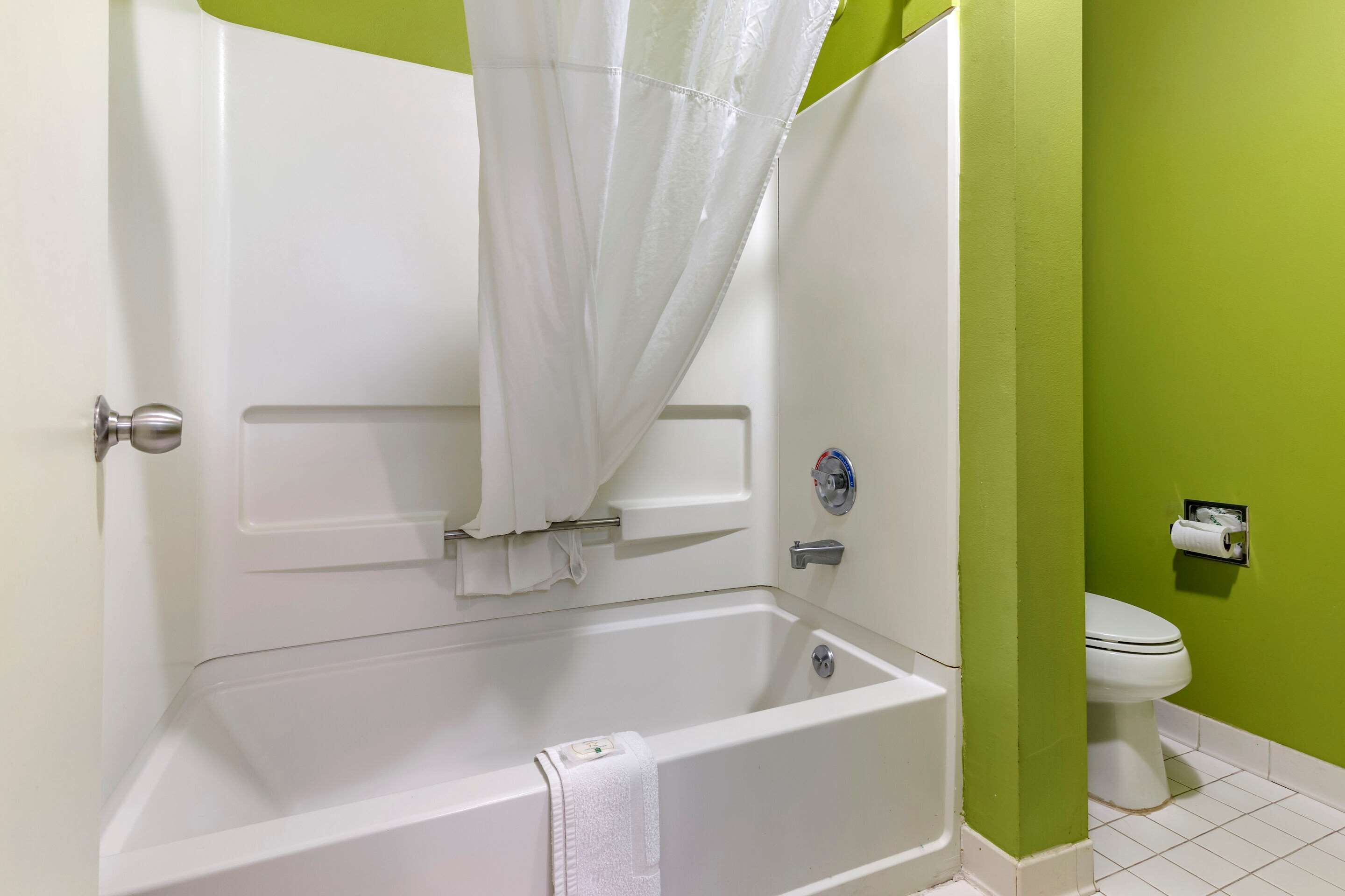 A bathroom with a bathtub, toilet, and green walls.