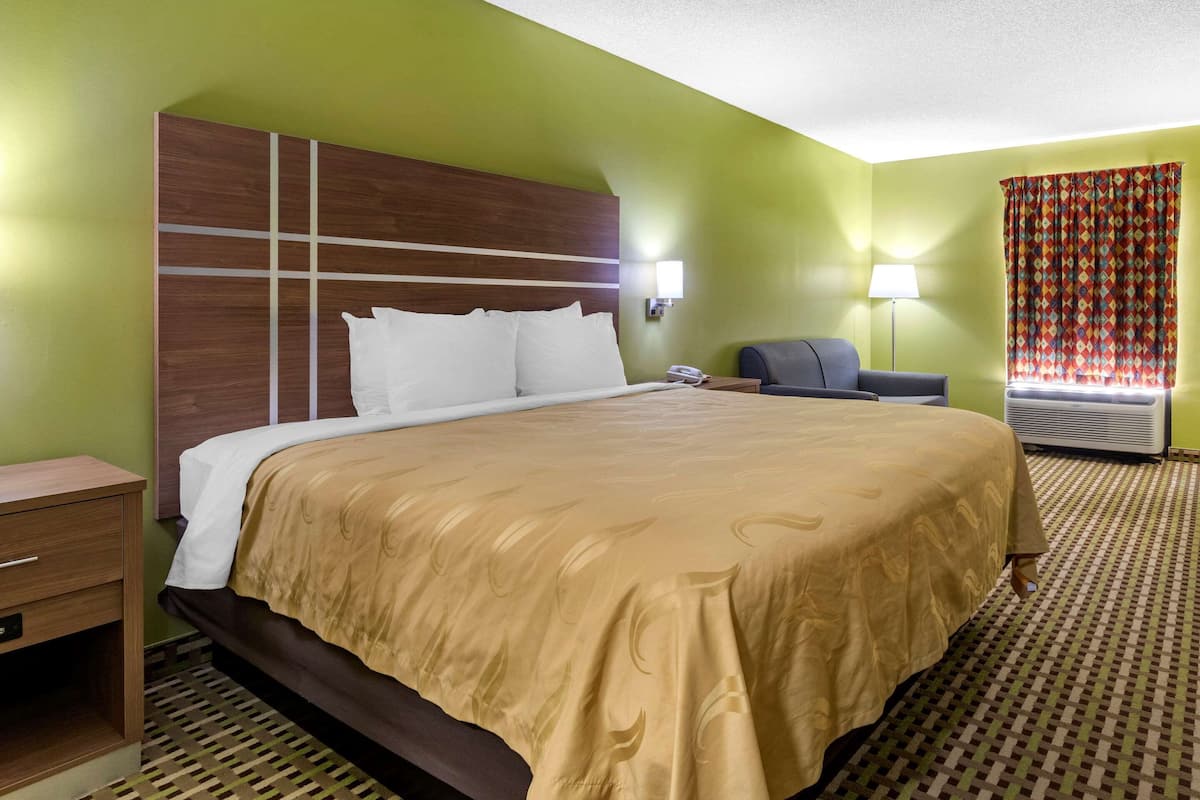 Una habitación de hotel con una cama grande, un escritorio, una silla, una lámpara y un ventanal con cortinas.