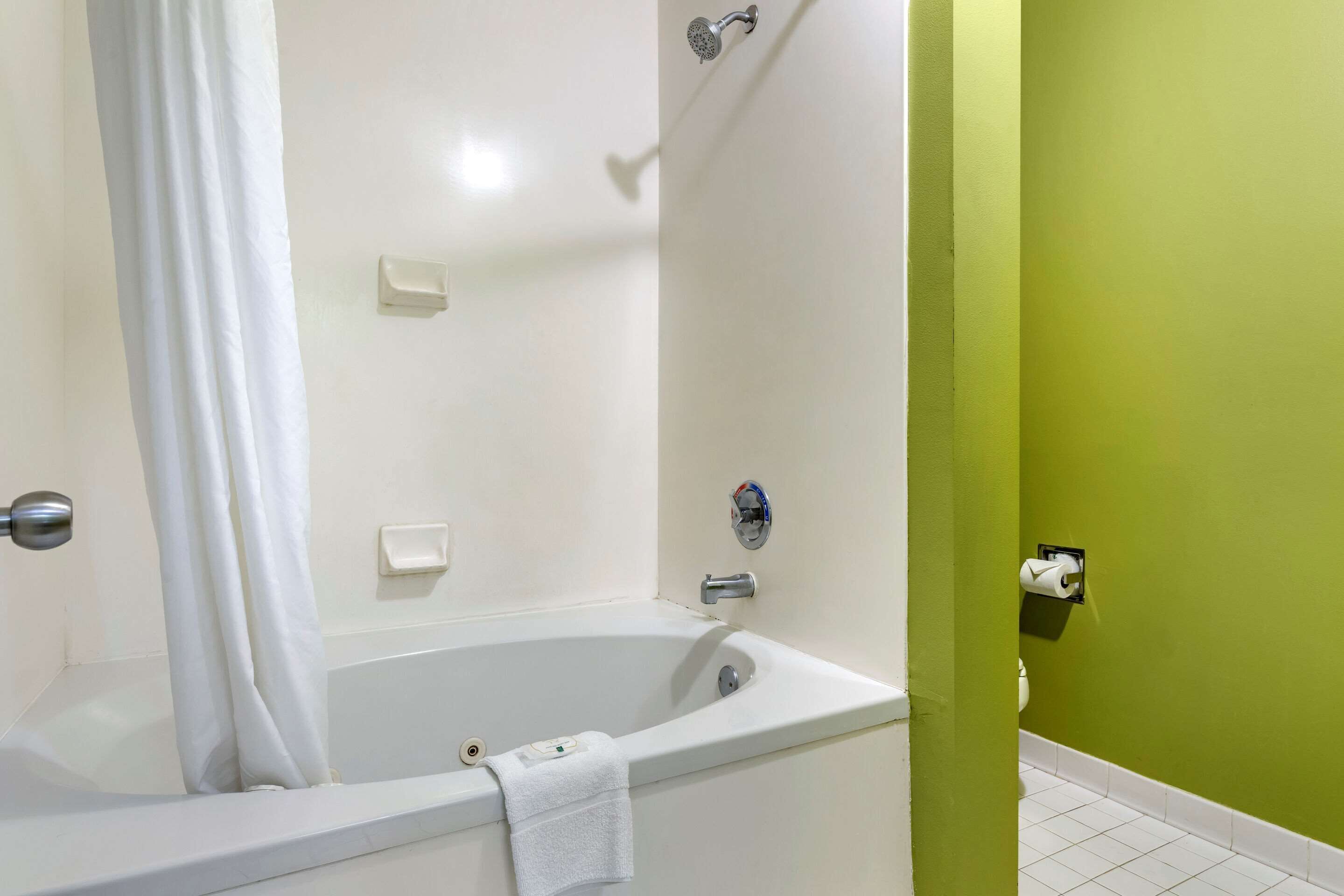 A bathroom with a bathtub, a shower curtain, a toilet, and a green wall.