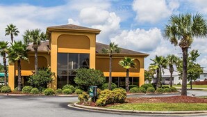 A yellow building with large windows and palm trees in front.