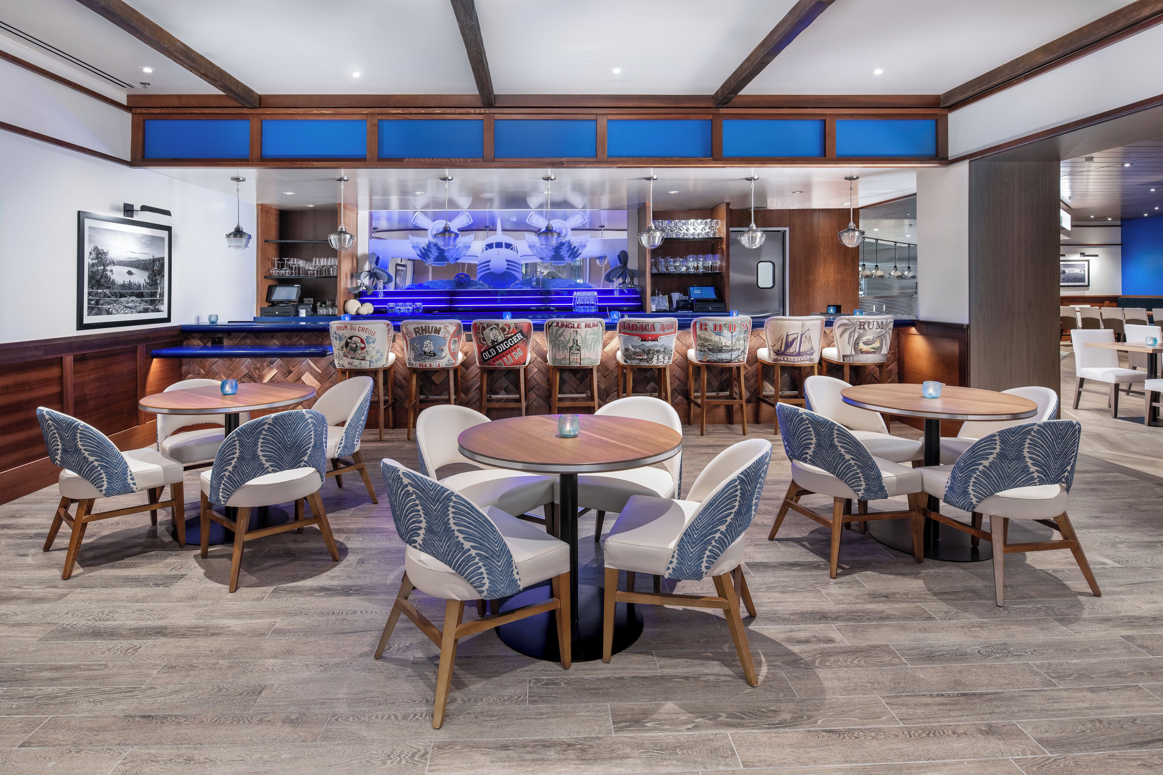 Eine moderne Bar mit blau beleuchteter Theke, Holzbalkendecke und einer Mischung aus Bar- und Essenshockern.