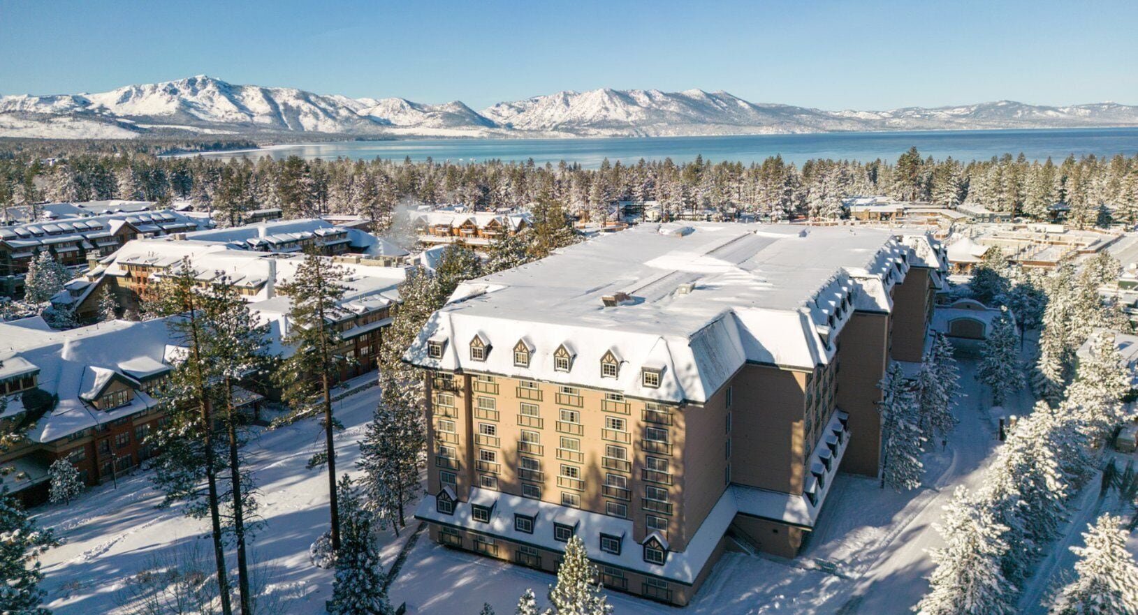A large hotel with multiple buildings, surrounded by snow-covered trees and mountains in the background.