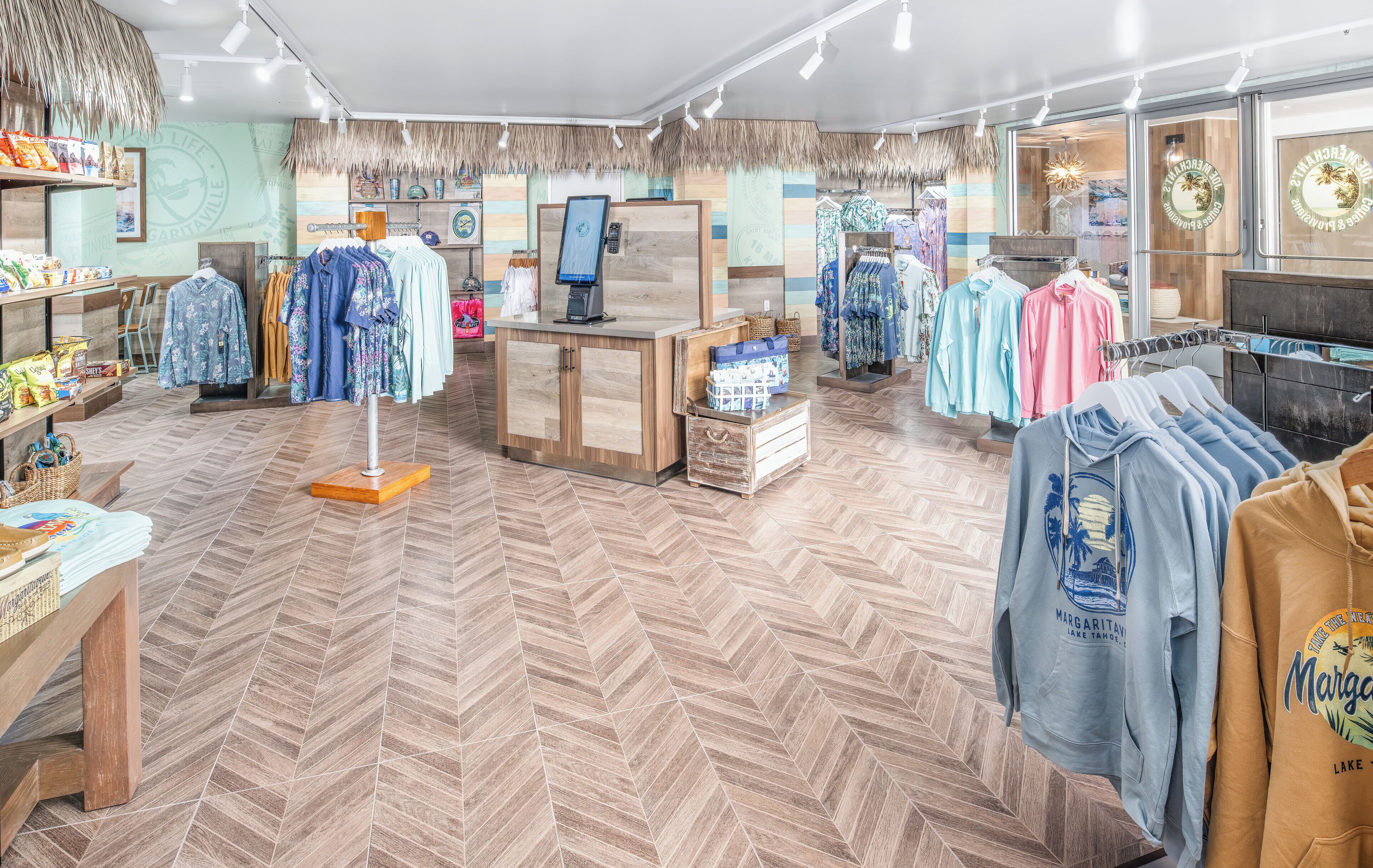 Negozio di abbigliamento con pavimento in legno, un bancone cassa e diversi espositori.