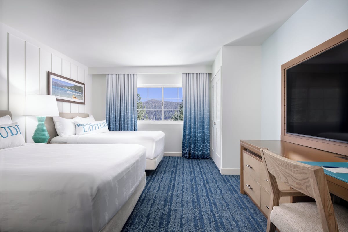 A hotel room with two beds, a desk, a TV, and a window with curtains.