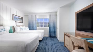 Quarto de hotel com duas camas, uma mesa, uma televisão e uma janela com cortinas.