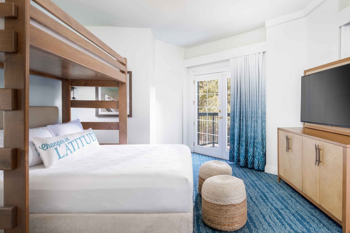 A hotel room with a bunk bed, a flat-screen TV, a wooden cabinet, and a large sliding glass door to the outside.
