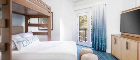 A hotel room with a bunk bed, a flat-screen TV, a wooden cabinet, and a large sliding glass door to the outside.