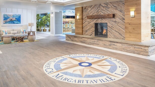A spacious lobby with a central fireplace, a circular emblem on the floor, and hanging glass chandeliers. - Margaritaville Resort Lake Tahoe (South Lake Tahoe)