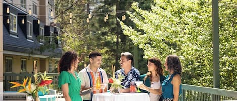 Un espace de restauration en plein air, avec des tables et des chaises, entouré de verdure et de bâtiments.