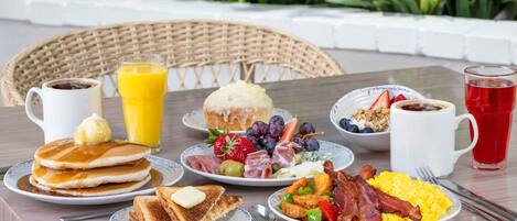 A breakfast table with pancakes, toast, fruit, eggs, bacon, and beverages.