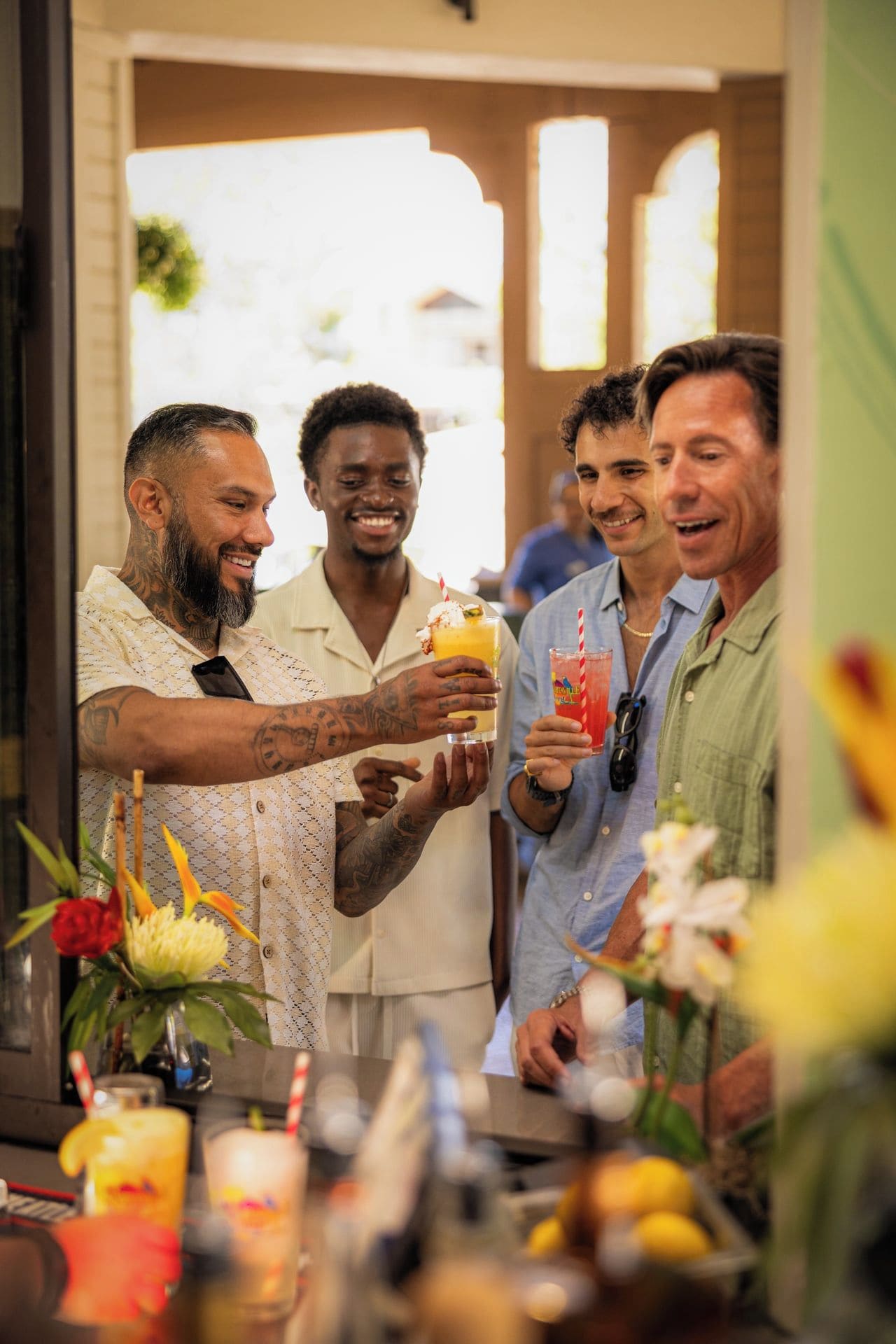Un groupe de personnes trinquant avec des boissons dans un bar où l’on propose une grande variété de breuvages, et où est disposé un arrangement floral.