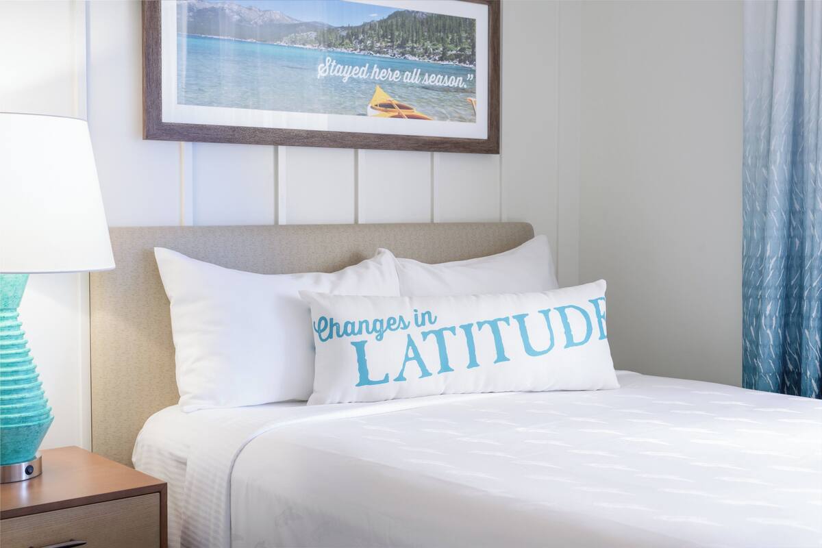 A neatly made bed with a pillow that reads "Changes in LATITUDE."