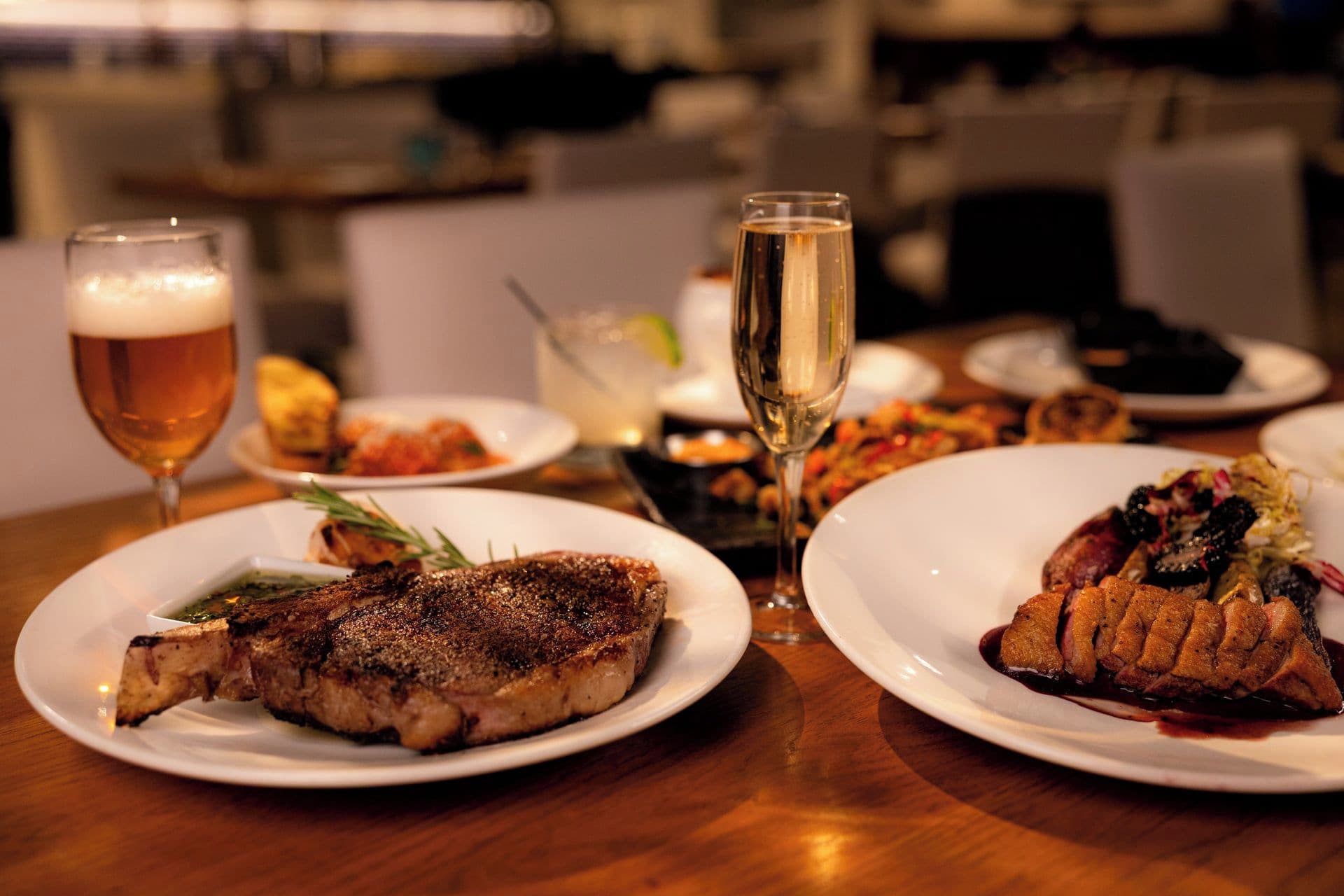 A dining table with plates of food, glasses of beer and wine, and a clear glass of water.