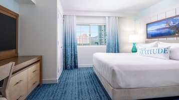 Habitación de hotel con cama, escritorio, silla, ventana con cortinas y vistas a edificios.