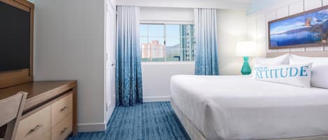 Habitación de hotel con cama, escritorio, silla, ventana con cortinas y vistas a edificios.