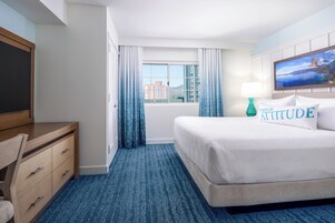 A hotel room with a bed, a desk, a chair, a window with curtains, and a view of buildings.