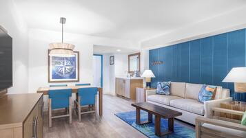 A modern living room with a sofa, coffee table, and dining area with chairs. There is a kitchen in the background.