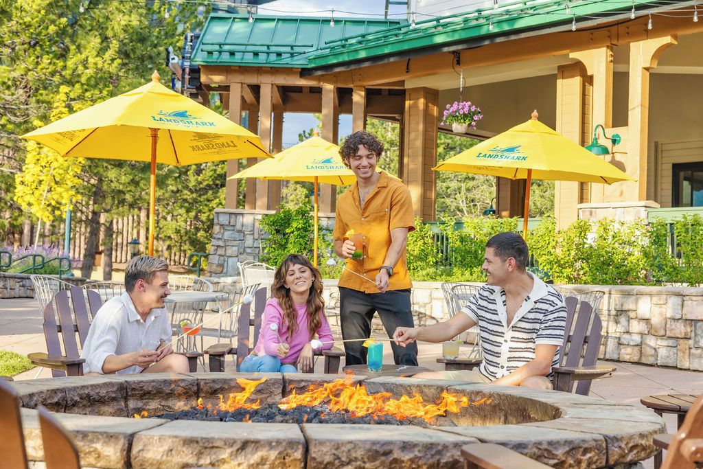An outdoor seating area with a fire pit, yellow umbrellas, and a building with a green roof in the background.