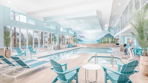 An indoor swimming pool area with lounge chairs and a view of a mountain landscape through large windows.