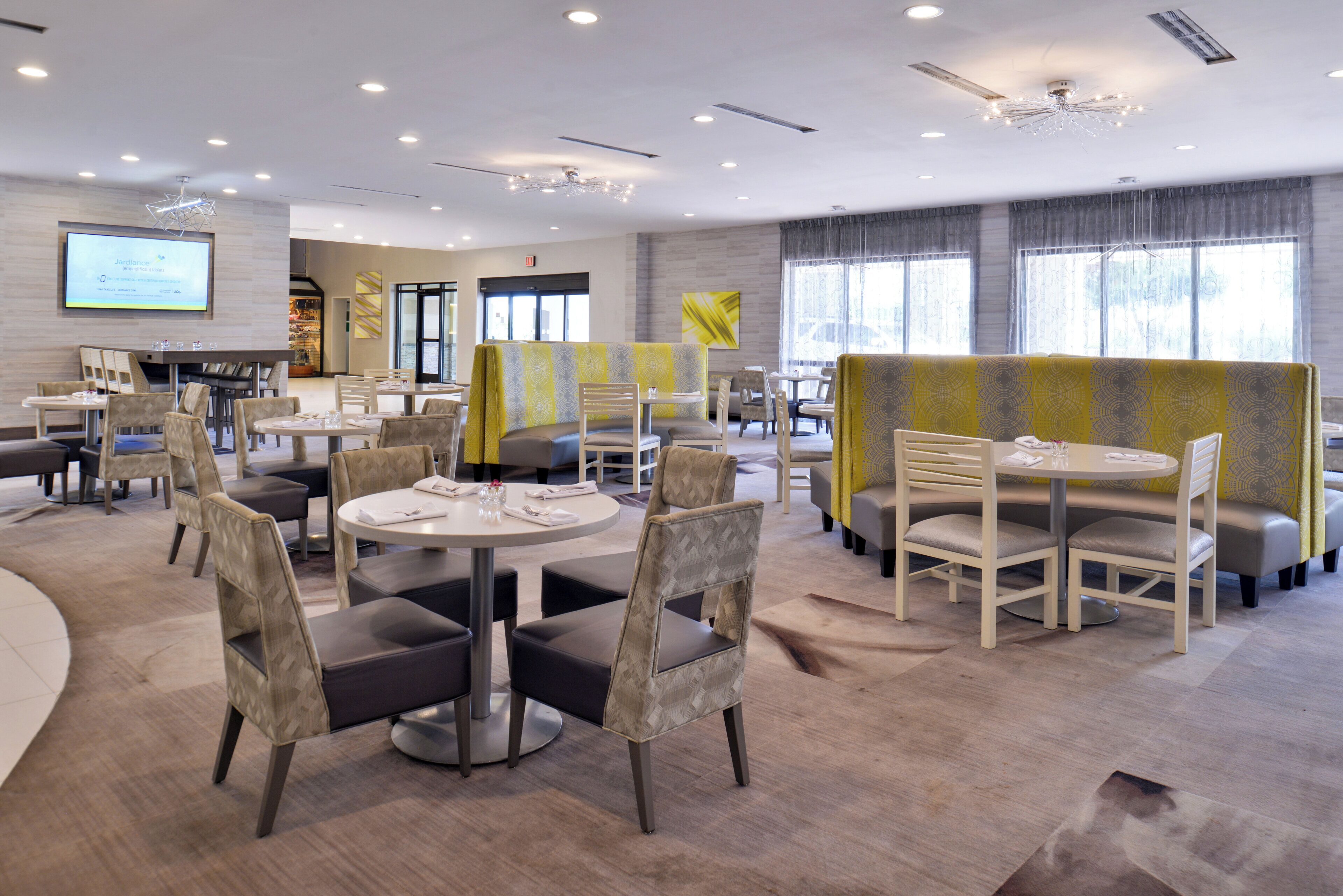 A modern dining area with round tables and chairs, a projection screen, and a large window.