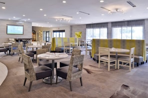 A modern dining area with round tables and chairs, a projection screen, and a large window. - Holiday Inn Dallas-Richardson by IHG (Richardson)