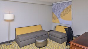 A hotel room with a sofa, ottoman, and a desk. - Holiday Inn Dallas-Richardson by IHG (Richardson)